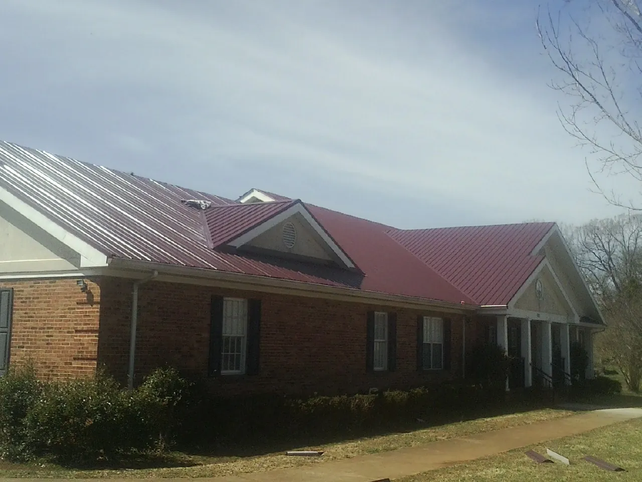 Red metal roof with gabled entries on a long brick building, from a Hail Damage Roof Repair job in Pinon Hills