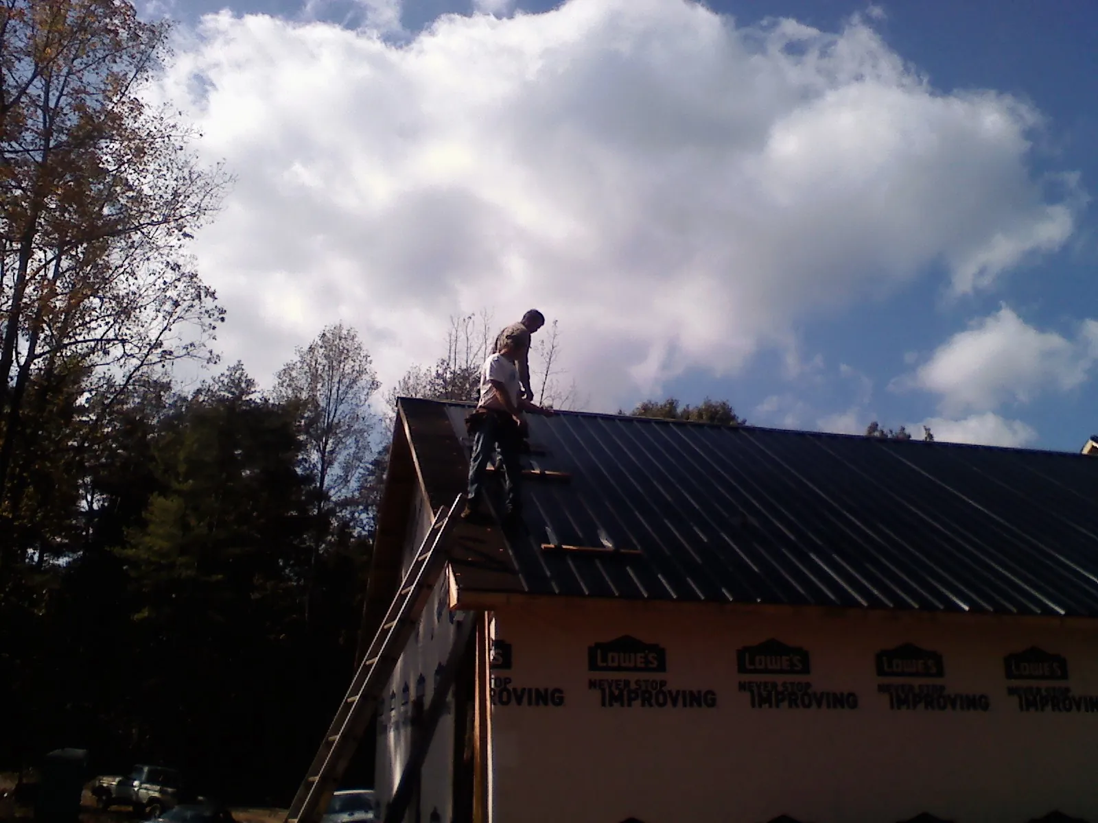 Roofer fastening dark metal panels high against a cloudy sky, from a Roof Inspection job in Pinon Hills